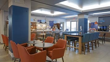 A modern cafe with round tables and orange chairs, a coffee bar, and a sign that says "MUST HAVE COFFEE."