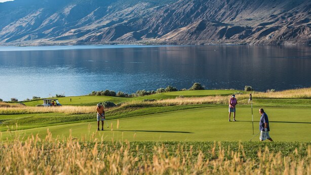 Un campo de golf con un lago y montañas al fondo.