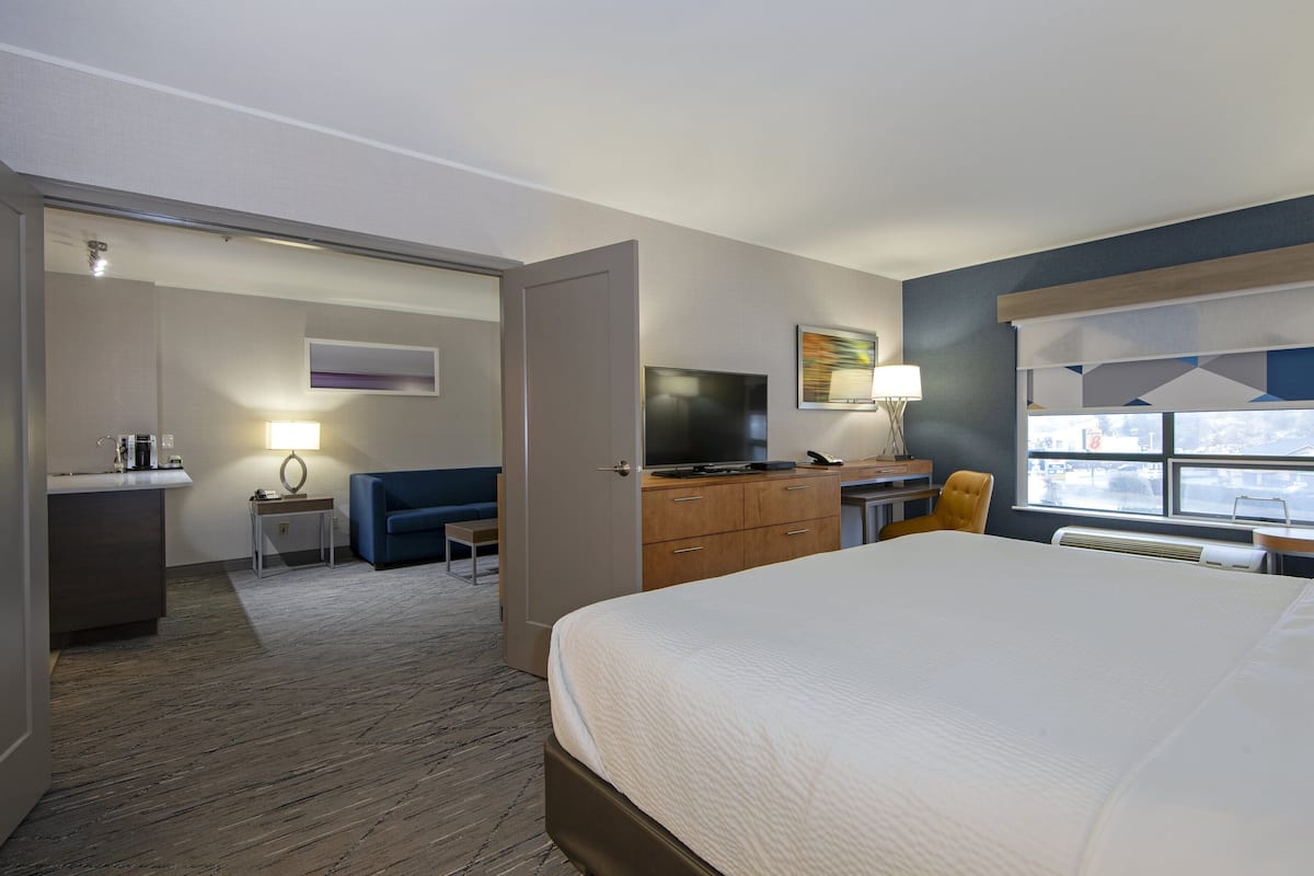 A hotel room with a large bed, a desk with a computer, a television, a sofa, and a window with a view of the outside.