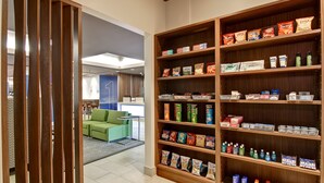 Un vestíbulo de hotel con una amplia estantería de madera repleta de aperitivos y artículos de aseo.