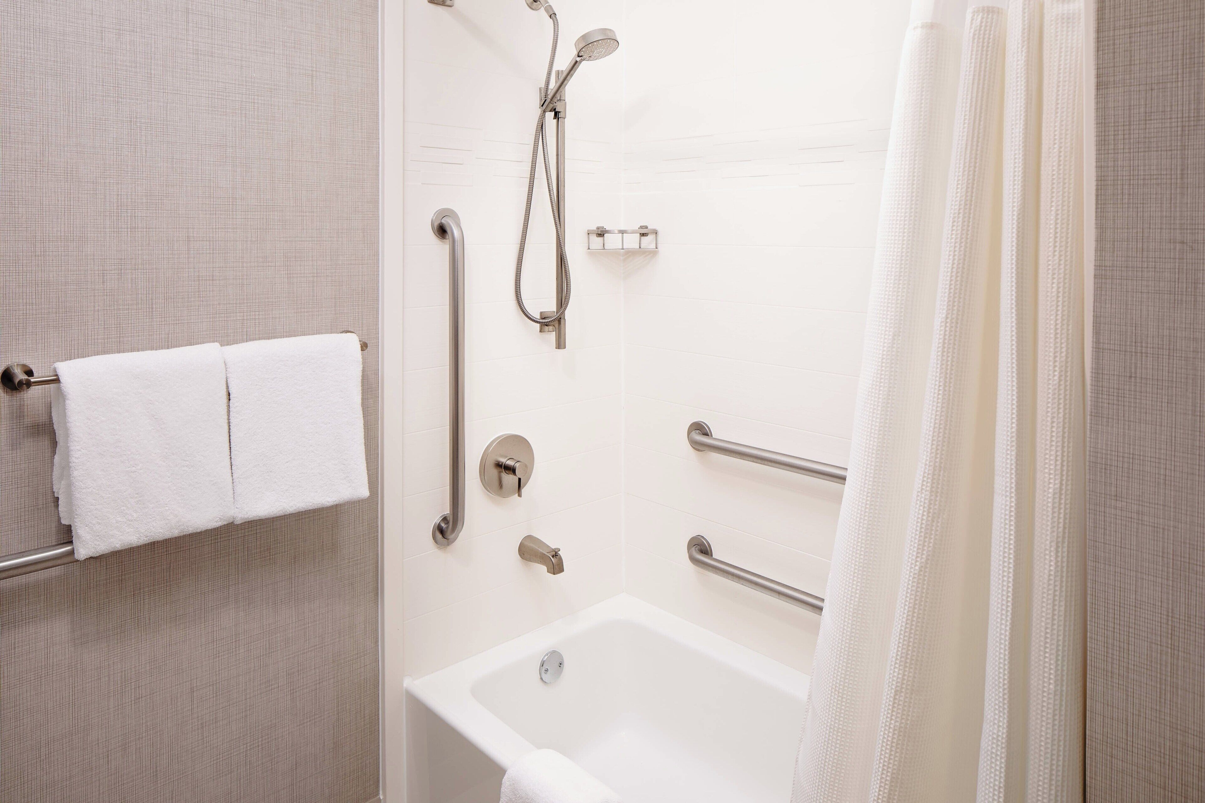 Un baño con bañera, barras de apoyo, toallero y cabezal de ducha.