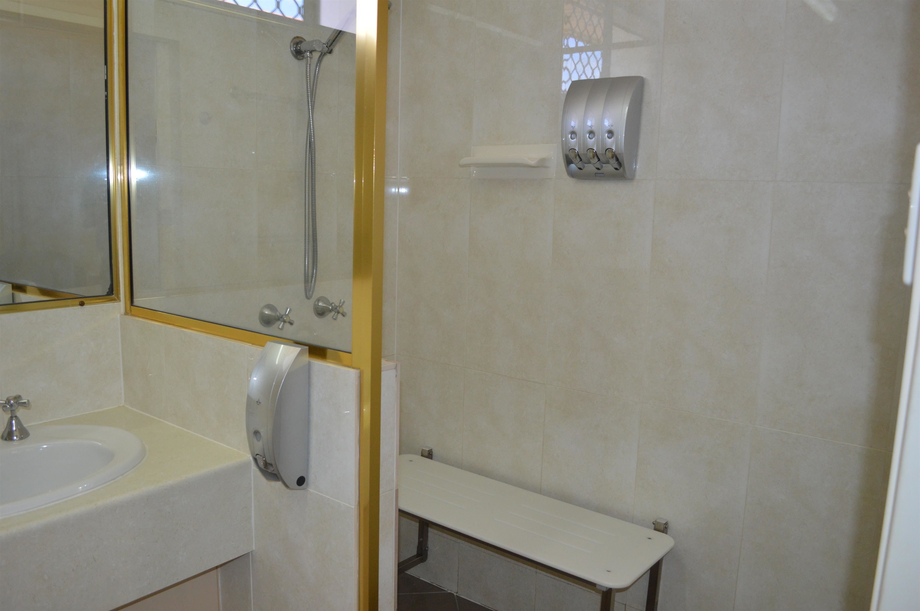 Un baño con lavamanos, espejo, ducha y dispensador de toallas.