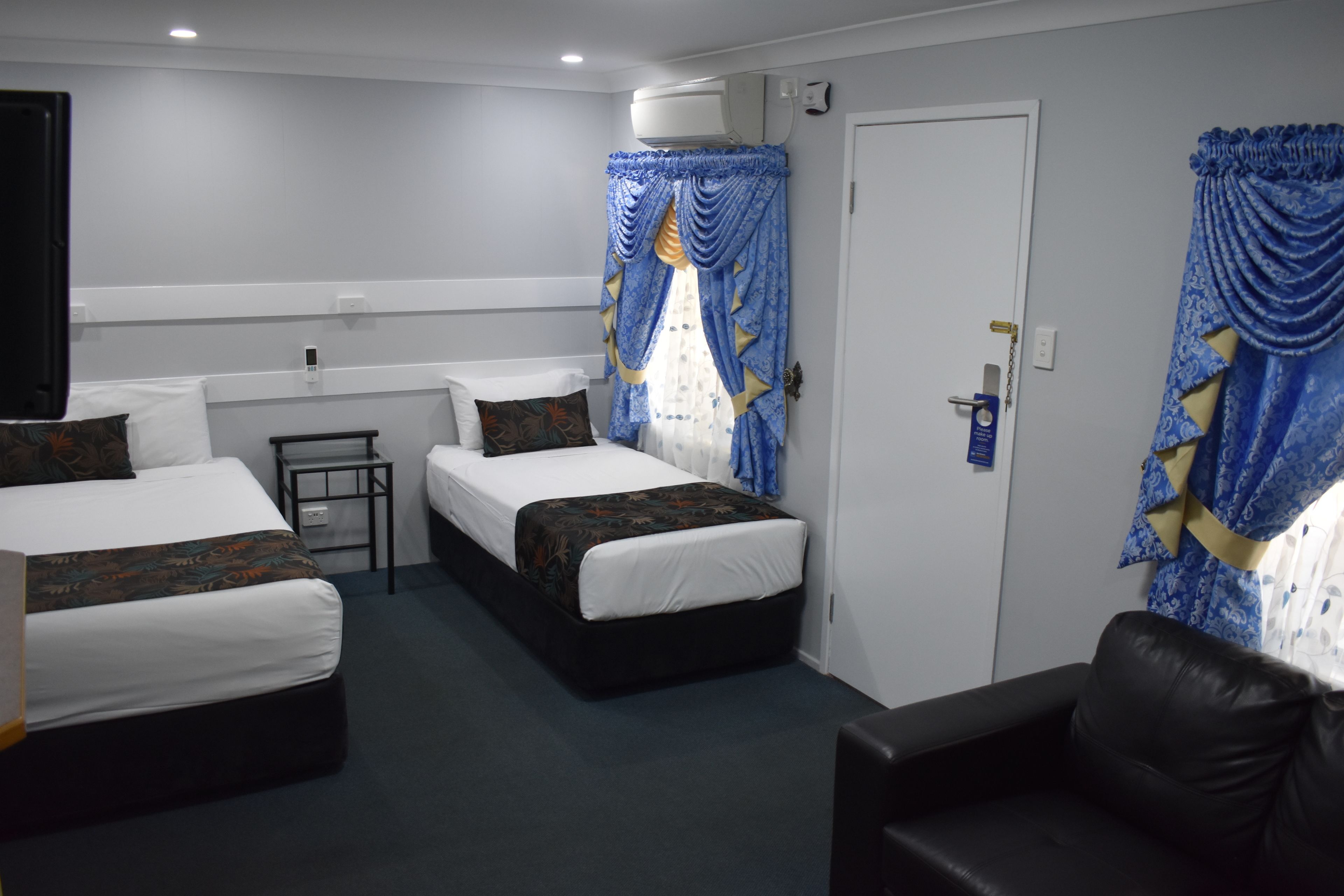 Une chambre d’hôtel avec deux lits simples, une petite table, un canapé et une porte avec un rideau.