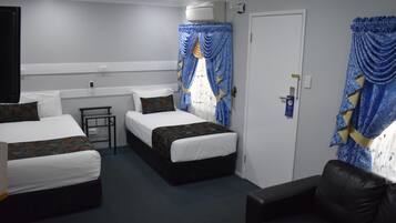 Une chambre d’hôtel avec deux lits simples, une petite table, un canapé et une porte avec un rideau.