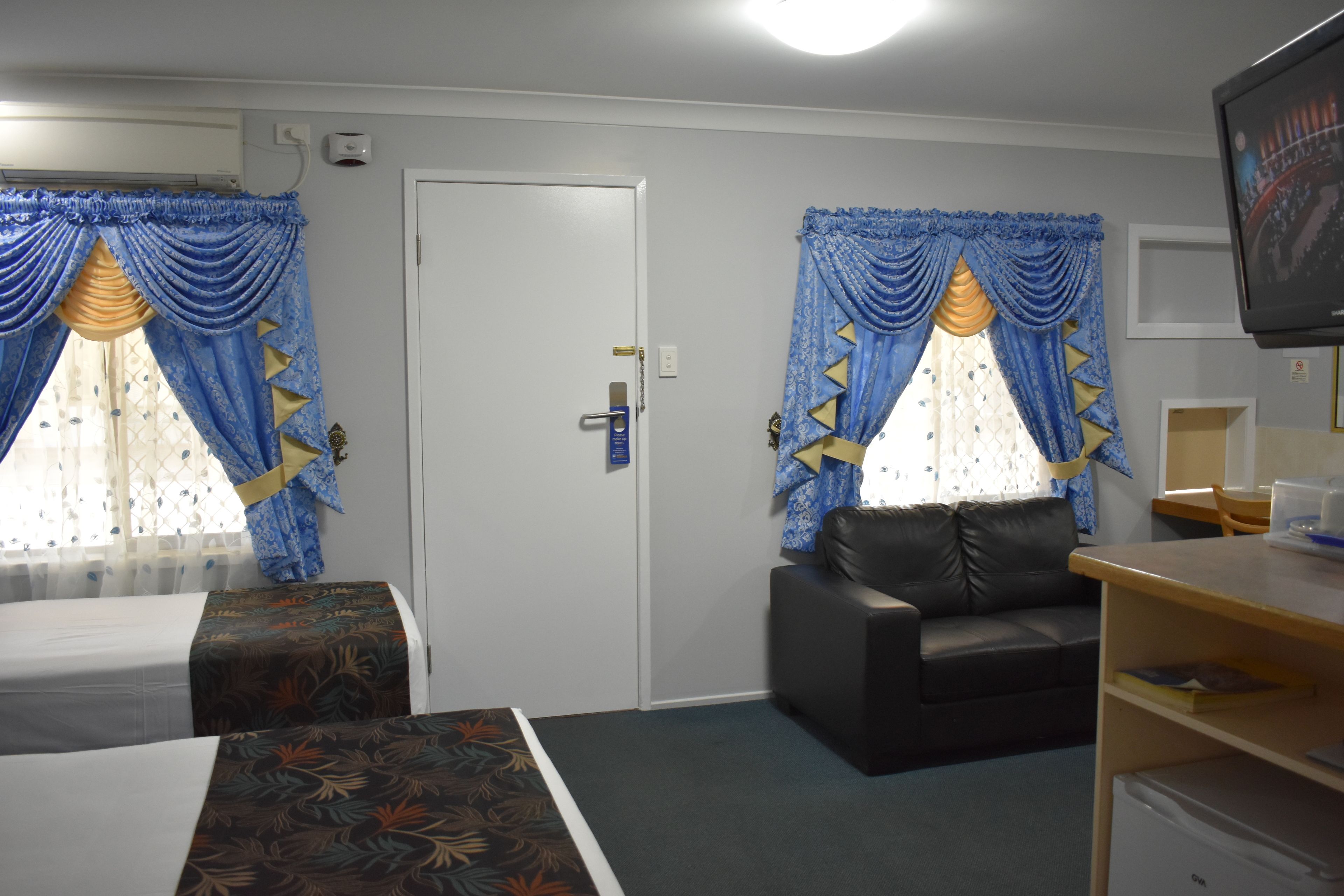 A hotel room with two beds, a sofa, a TV, and a door.