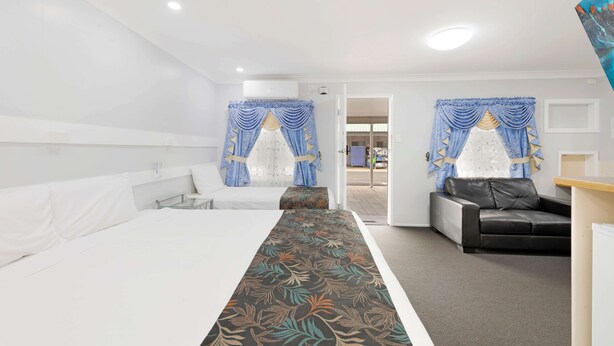Una habitación de hotel con una cama grande, un escritorio, una silla y dos ventanas con cortinas.