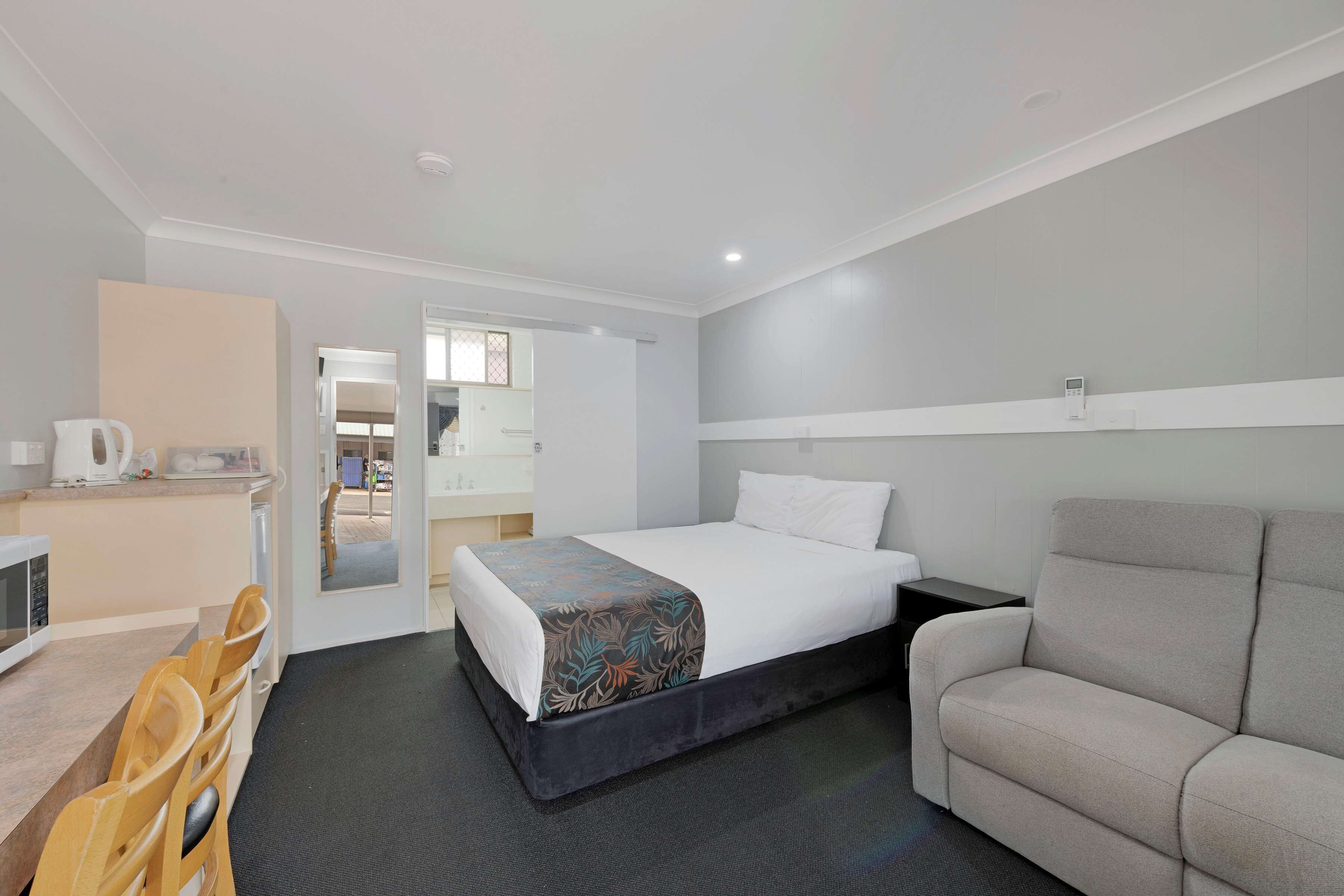 A hotel room with a bed, a sofa, a desk with a chair, and a mirror.