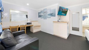Una habitación de hotel compacta con sofá, escritorio con microondas, kitchenette pequeña y televisor montado en la pared.