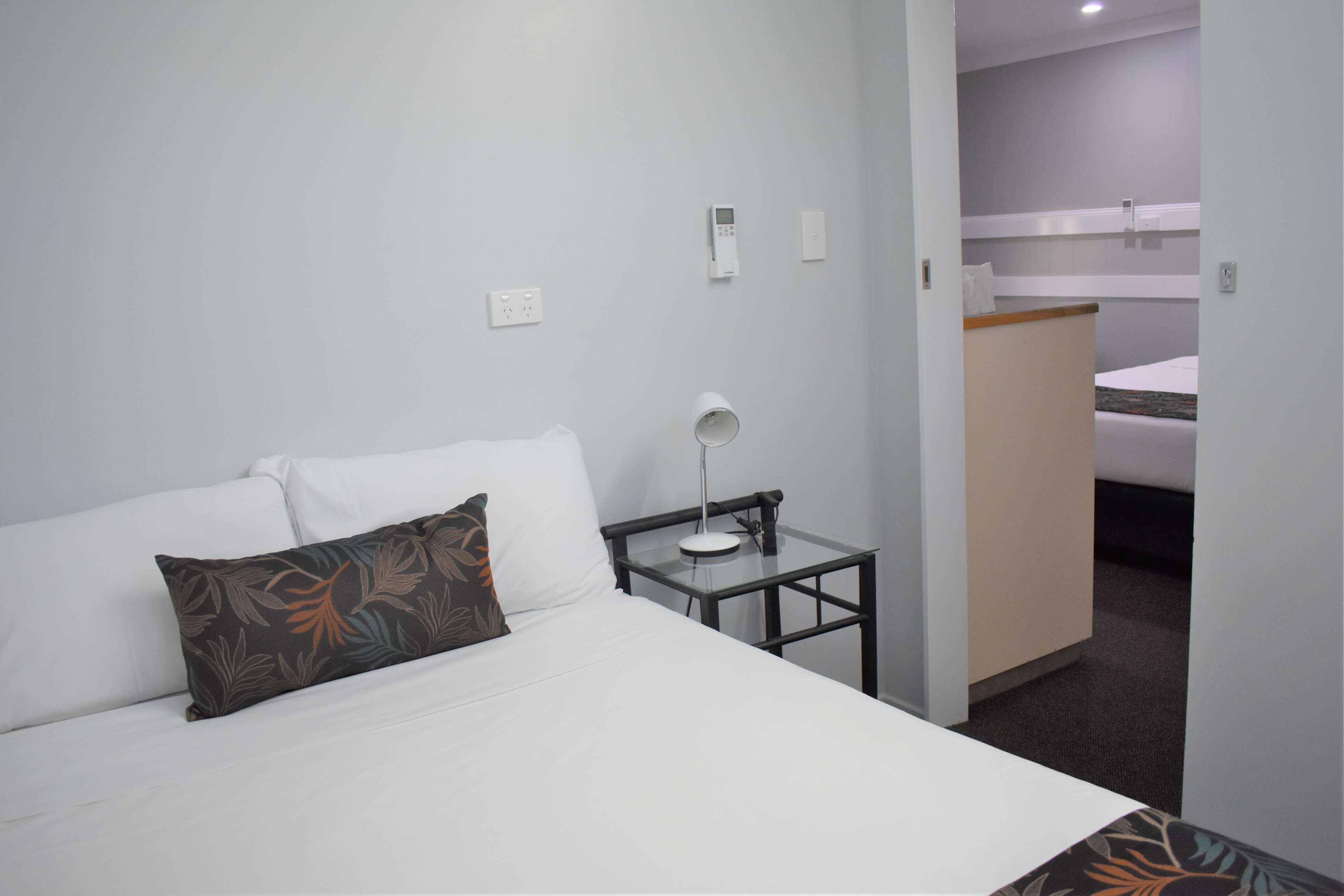 A hotel room with a bed, a bedside table with a lamp, a power outlet, and a wall socket.