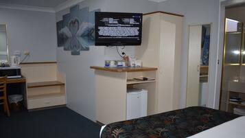 A hotel room with a bed, a desk with a computer, a television mounted on the wall, and a wardrobe.