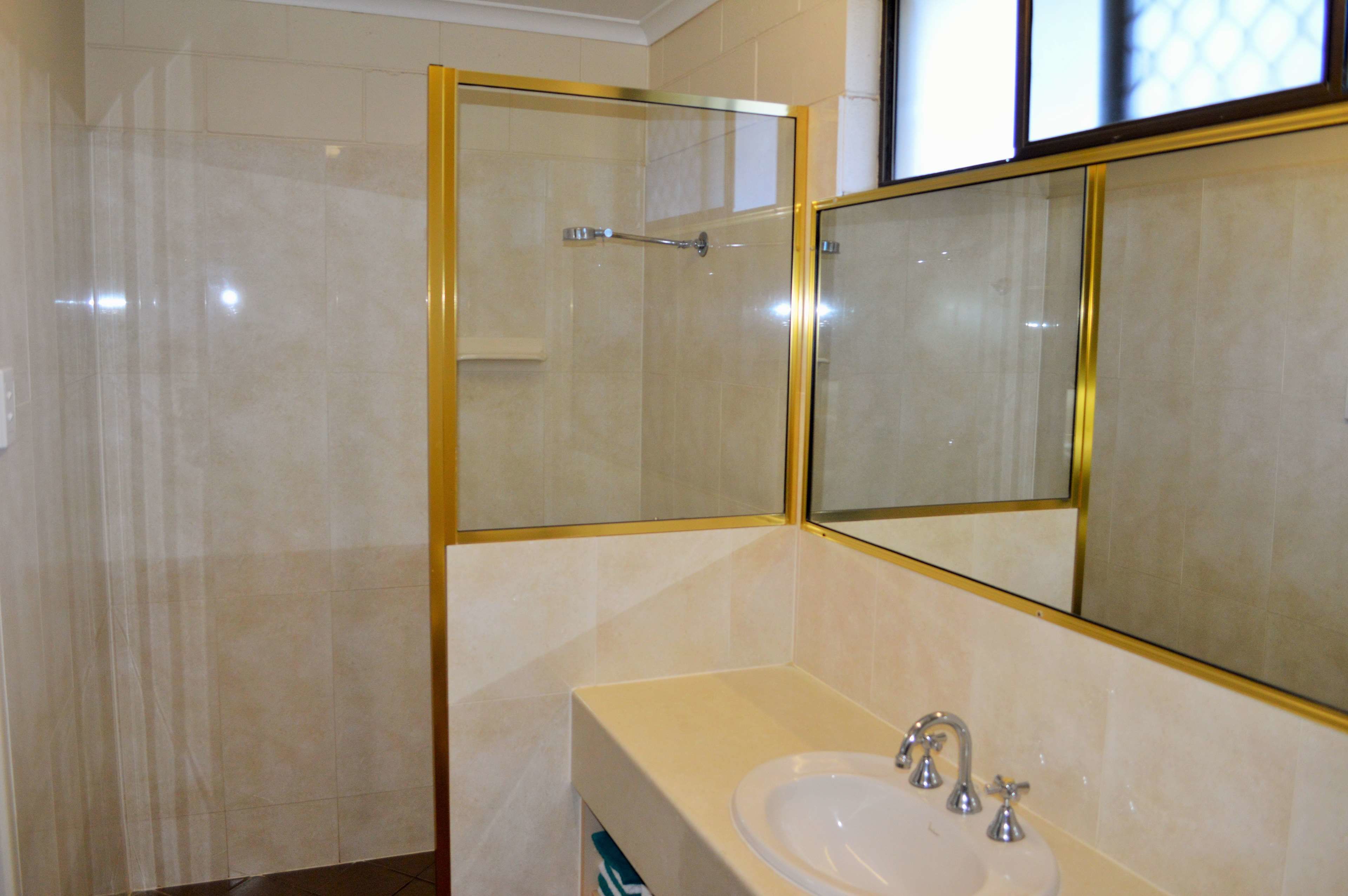 A bathroom with a glass-enclosed shower, a large mirror, and a sink with two faucets.