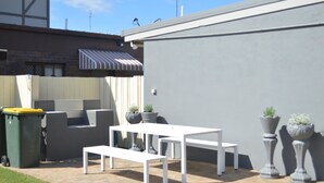 Un patio con mesa y banco blancos, plantas en macetas y un toldo a rayas.