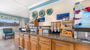 A kitchen with granite countertops, wooden cabinets, a coffee machine, and a fruit display.
