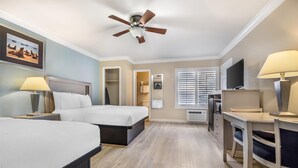 A hotel room with two beds, a desk, a TV, and a ceiling fan.