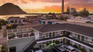 A coastal hotel with a rooftop bar, multiple balconies, and a view of the sea and a mountain.