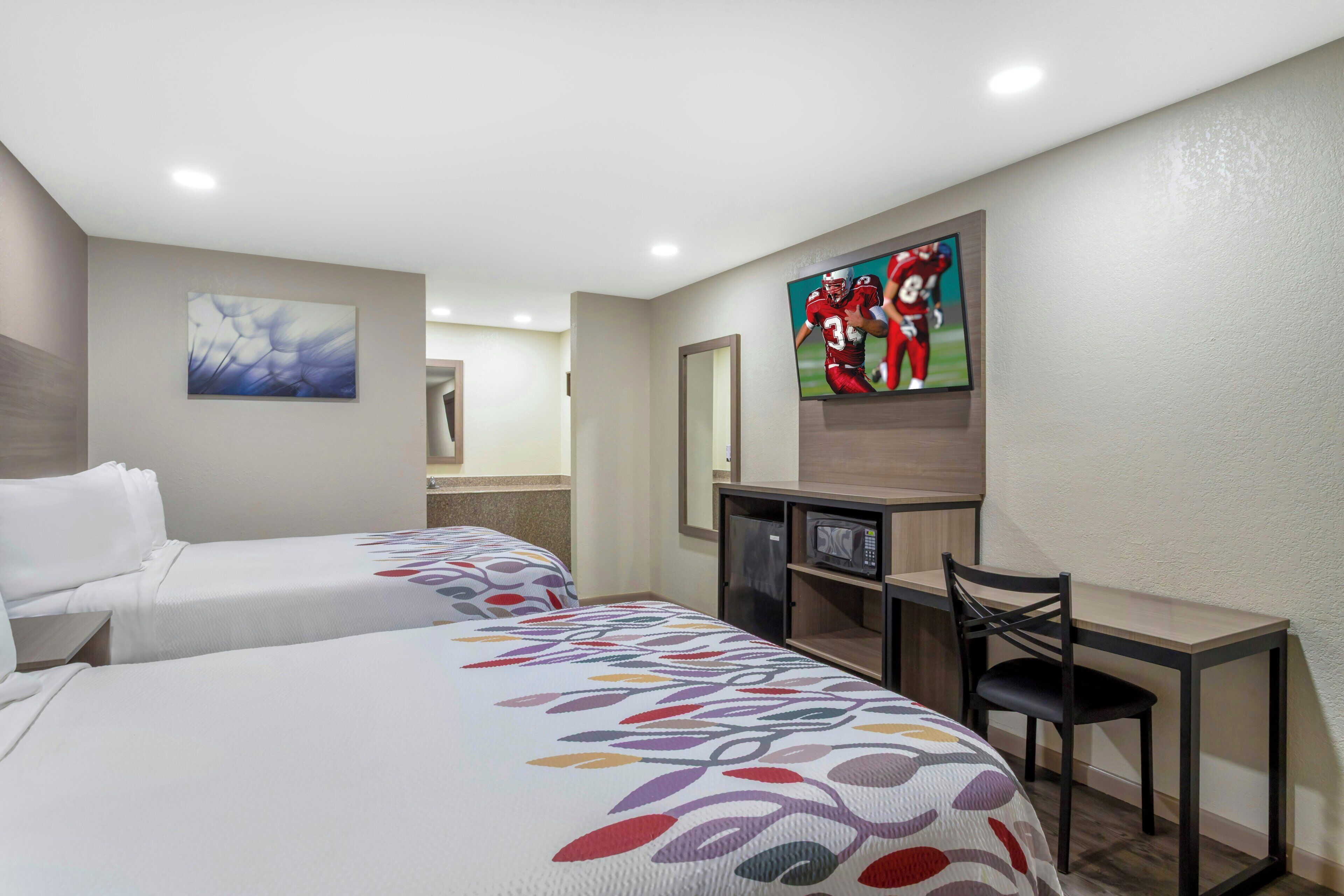 A hotel room with two beds, a desk, a chair, a TV, and artwork on the walls.