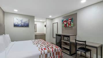 Ein Hotelzimmer mit Bett, Schreibtisch, Stuhl, Kühlschrank und Bildern an den Wänden.