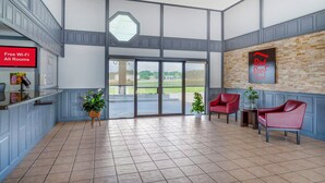 Vestíbulo de hotel con una recepción, un letrero de Red Roof, un ventanal grande y una zona de estar con sillas.