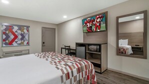 A hotel room with a bed, a TV mounted on the wall, a desk with a chair, and a small refrigerator. - Red Roof Inn Nacogdoches (Nacogdoches)