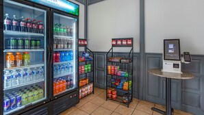 Un enfriador de bebidas repleto de varias opciones, un estante con aperitivos y un quiosco de autoservicio.