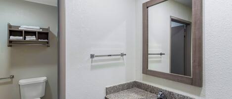 A bathroom with a toilet, a sink with a granite countertop, a towel rack, and a mirror.
