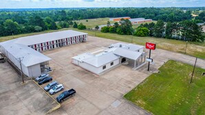 An aerial view of a parking lot with several cars, a building with a red roof, and a sign for 'Red Reef Resort.' - Red Roof Inn Nacogdoches (Nacogdoches)
