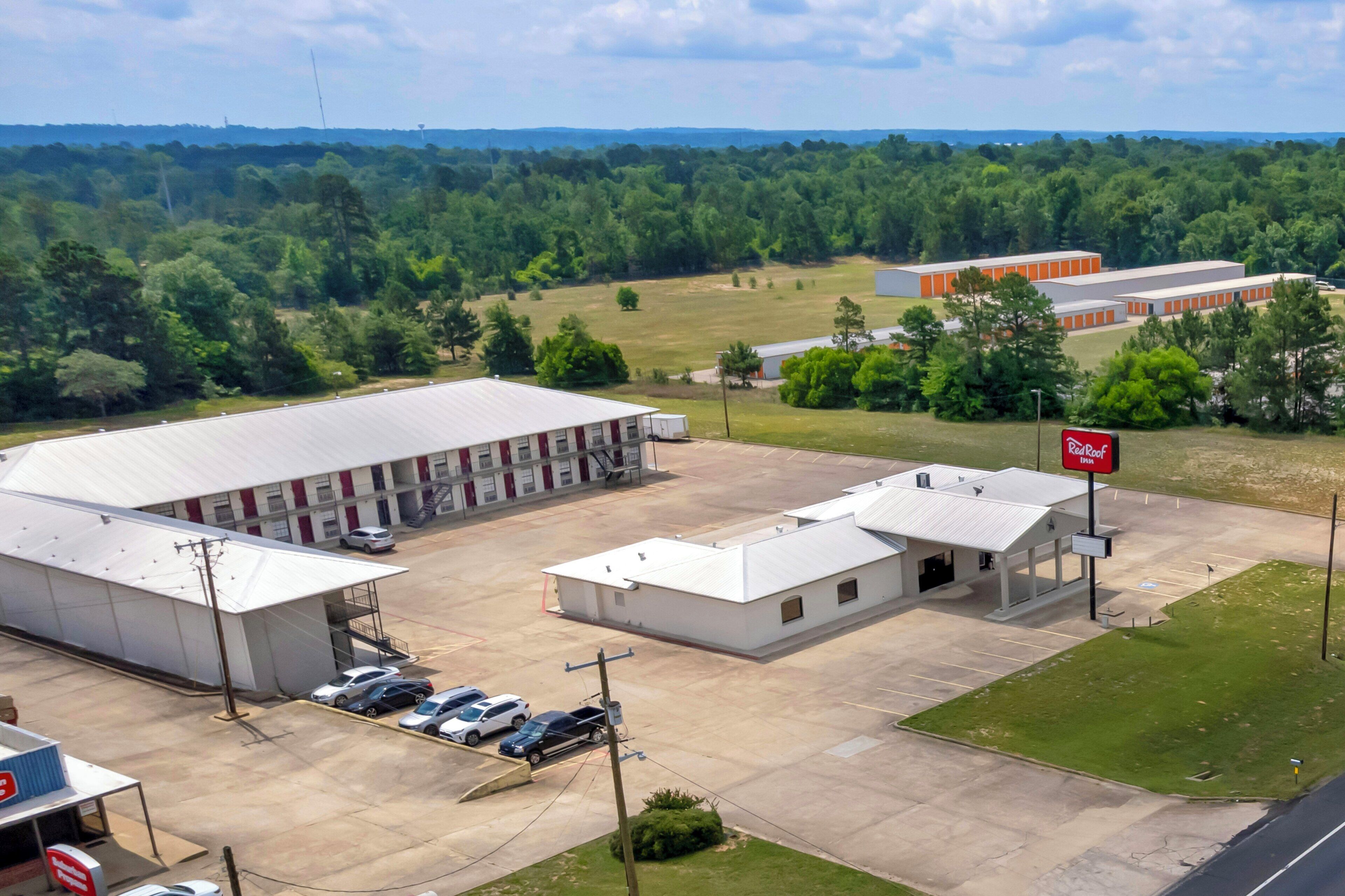 A large industrial building with a parking lot, a gas station, and a red sign.