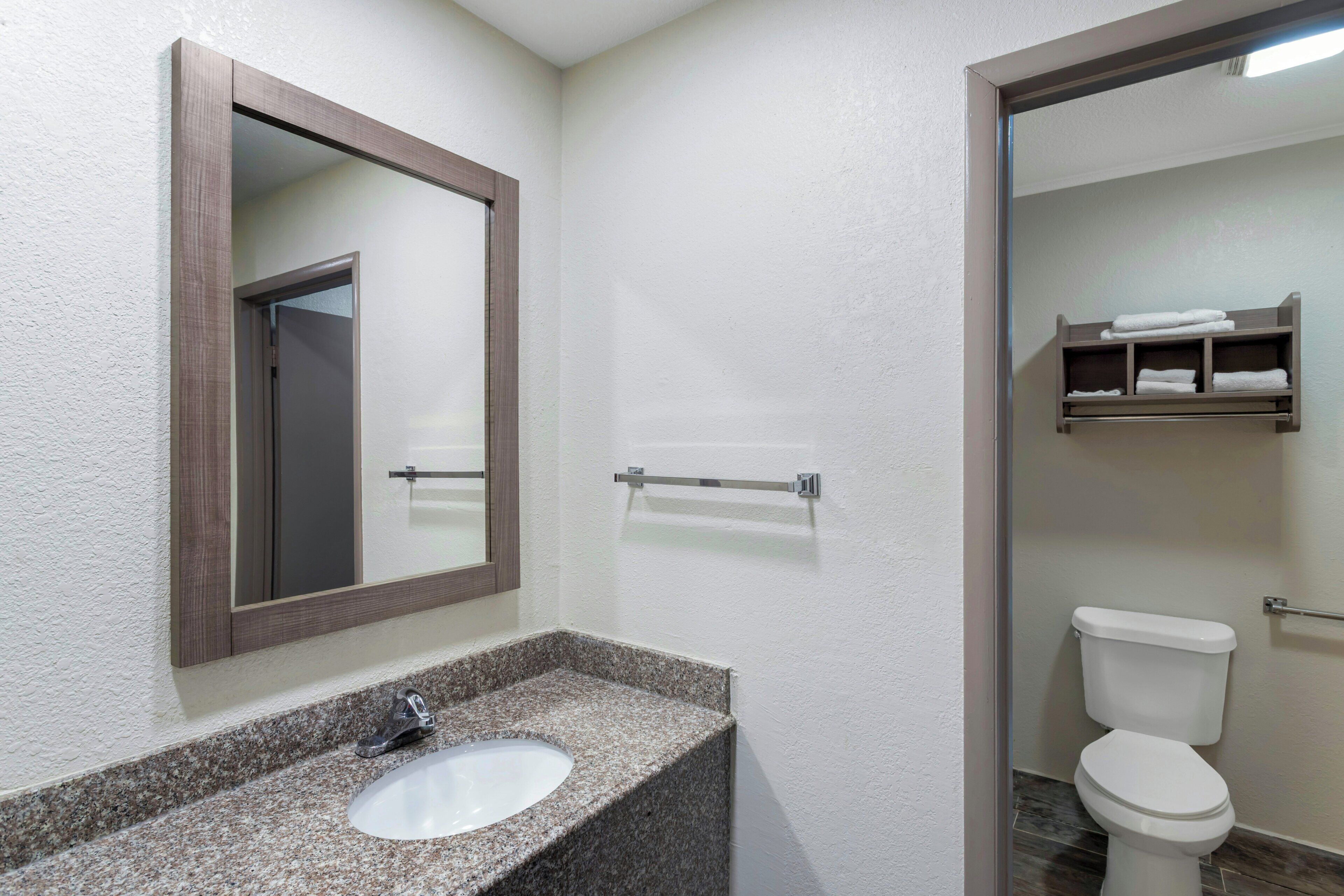Une salle de bain avec un lavabo doté d’un plan de travail en granit, un miroir, des toilettes et un porte-serviettes.