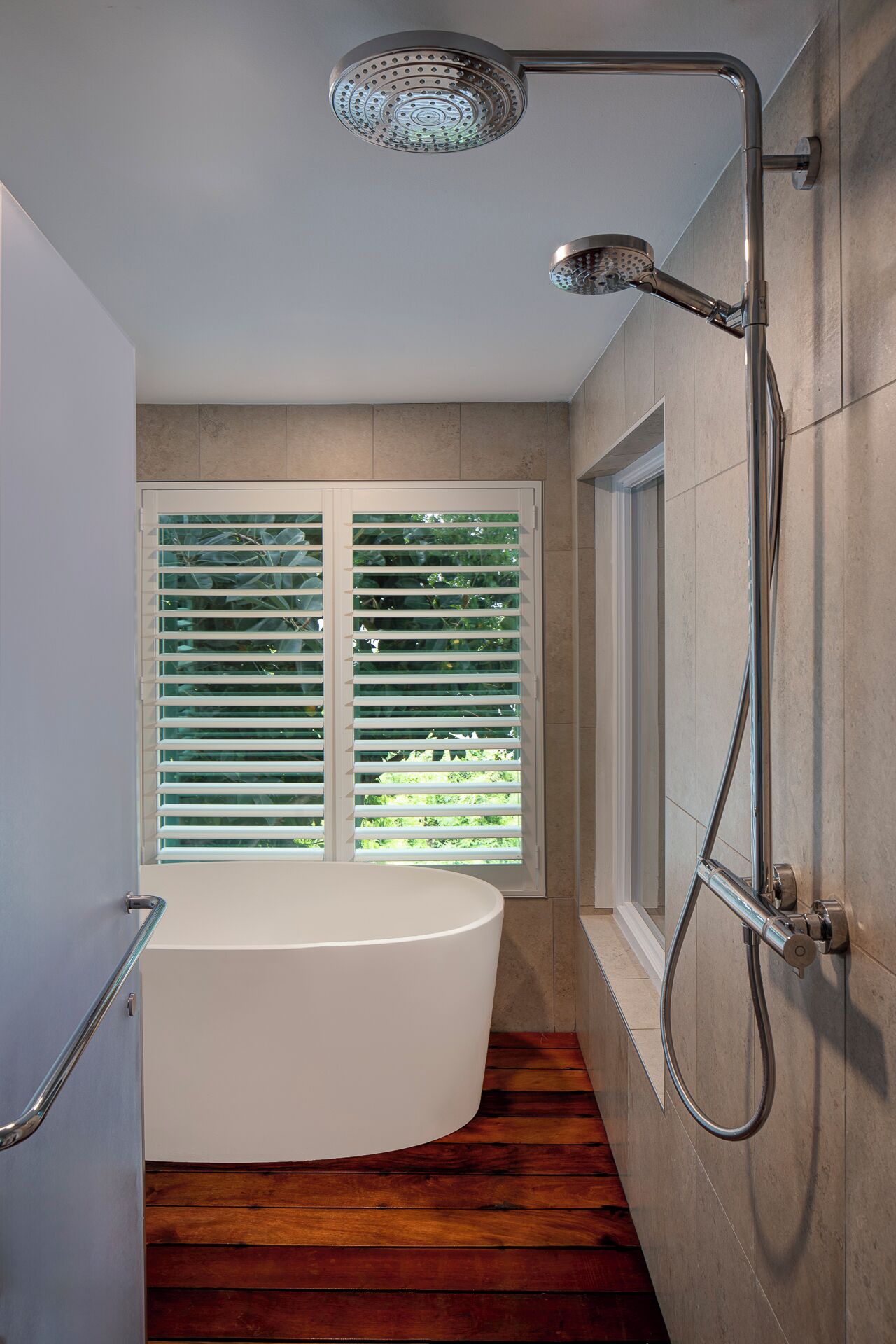 Un baño moderno con una bañera independiente, un cabezal de ducha y una ventana con persianas.