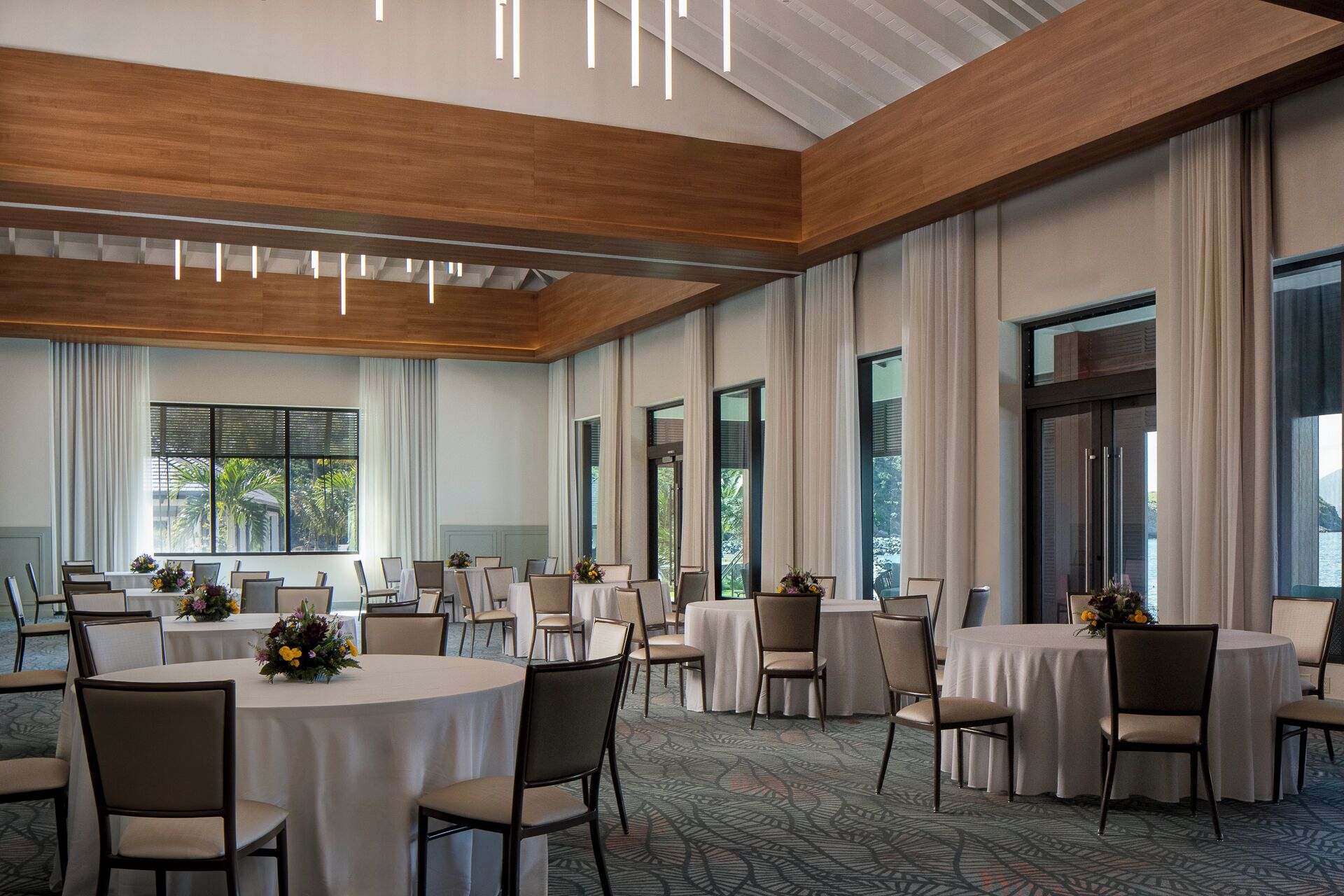 A spacious conference room with multiple tables and chairs, large windows, and a modern ceiling design.