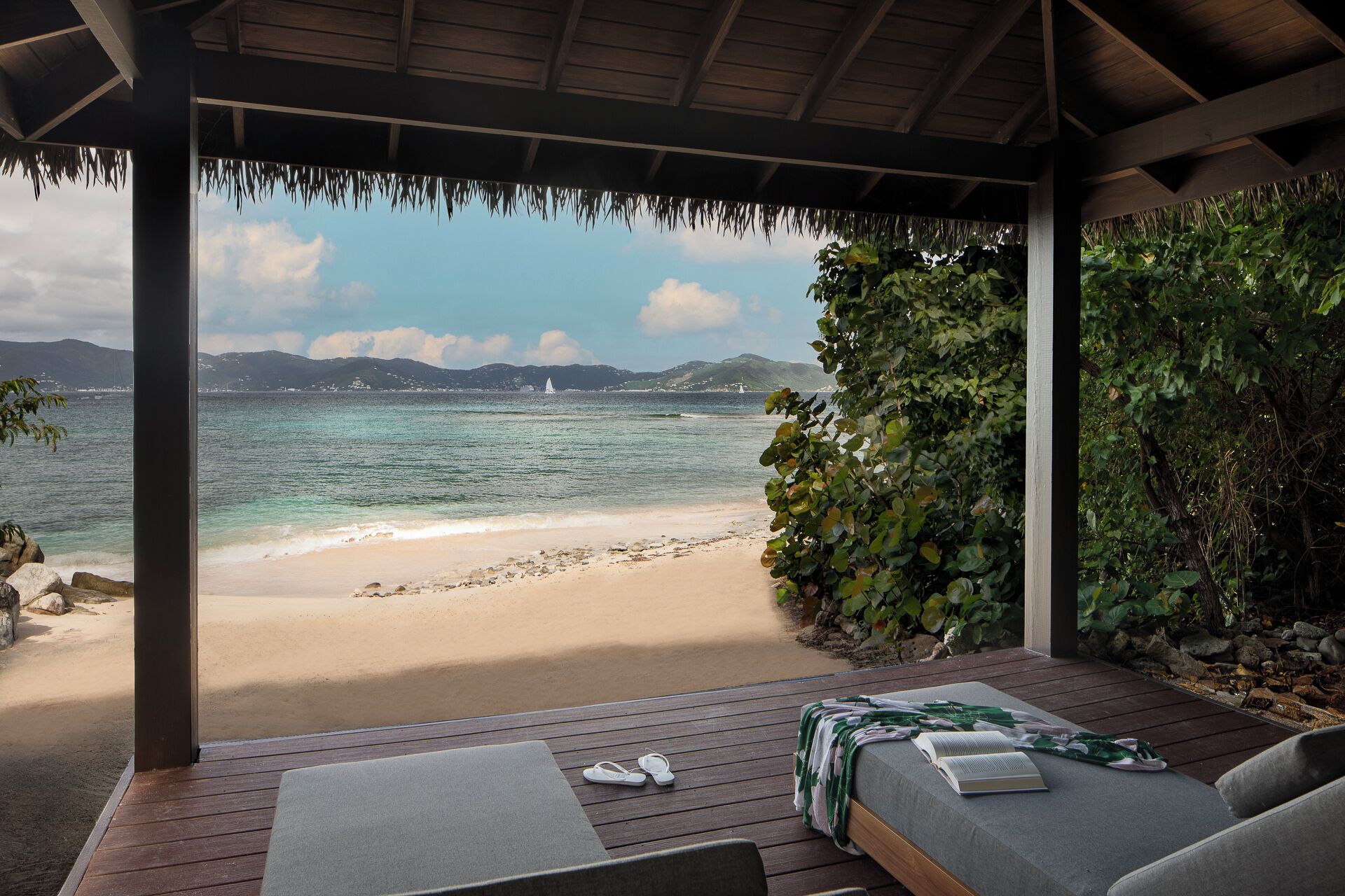 A covered outdoor seating area with a view of a beach and the sea.
