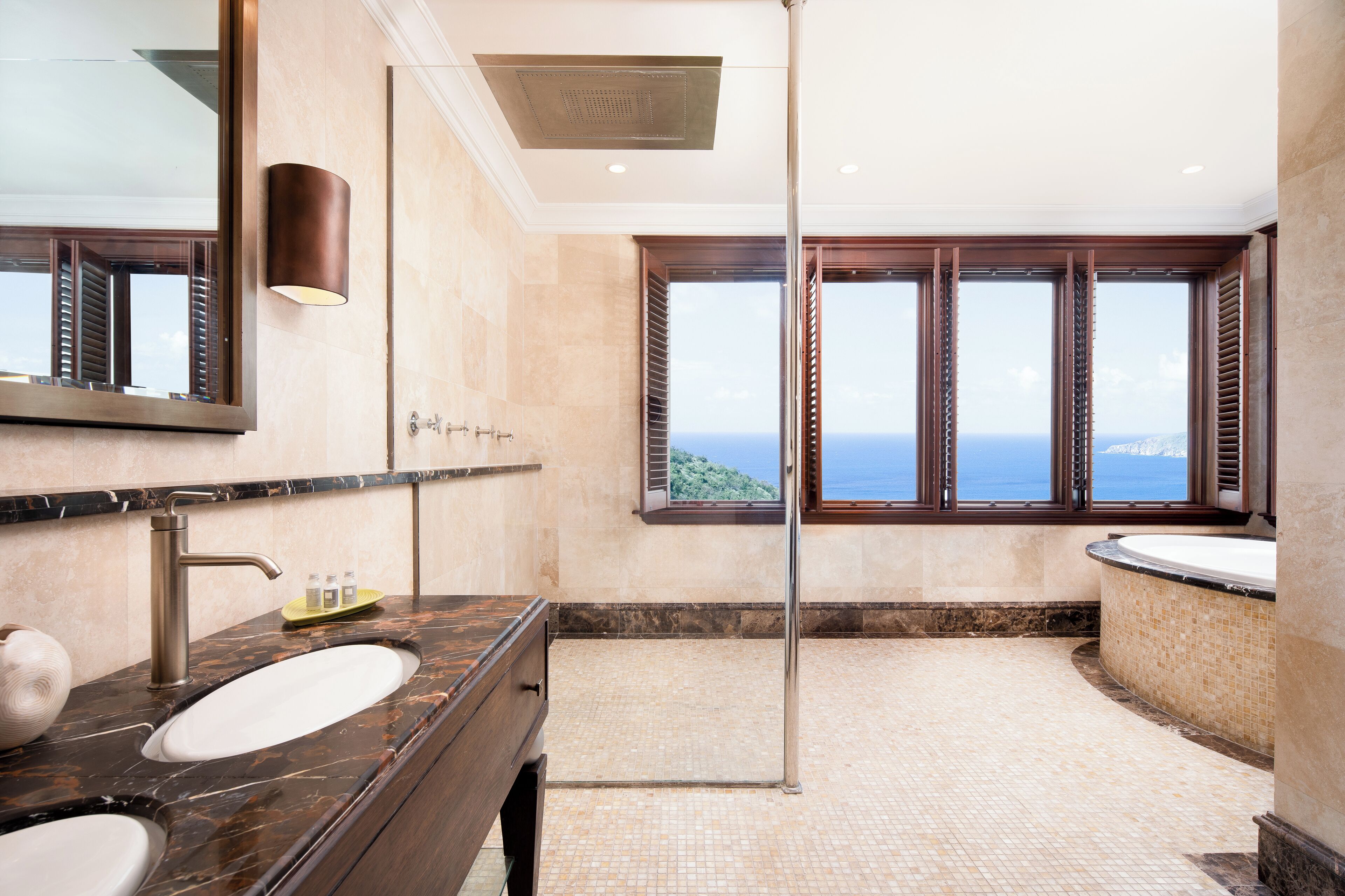 A modern bathroom with a large sink, a shower, and a view of the ocean.