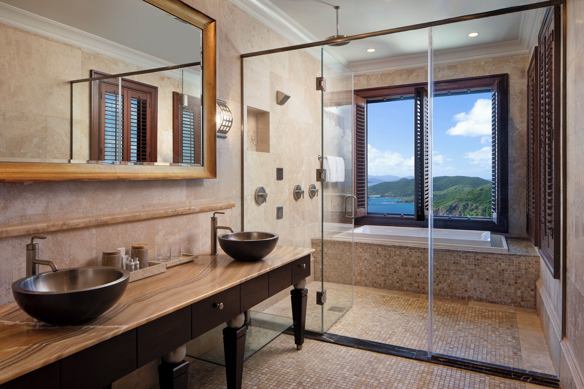 A modern bathroom with a large mirror, wooden vanity, a bowl sink, and a glass-enclosed shower with a view of the sea.