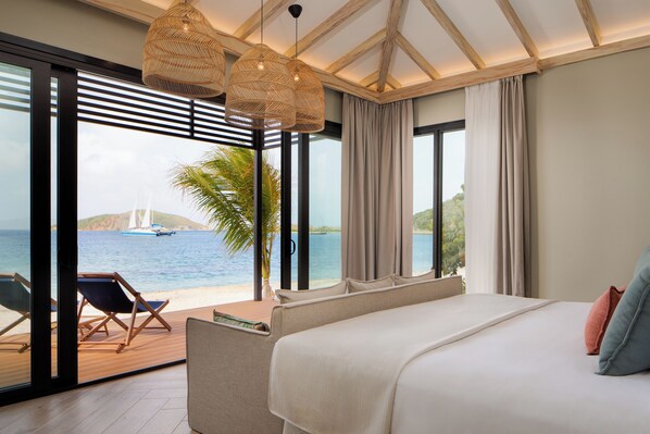 A bedroom with a large bed, a view of the sea, and a balcony with chairs.