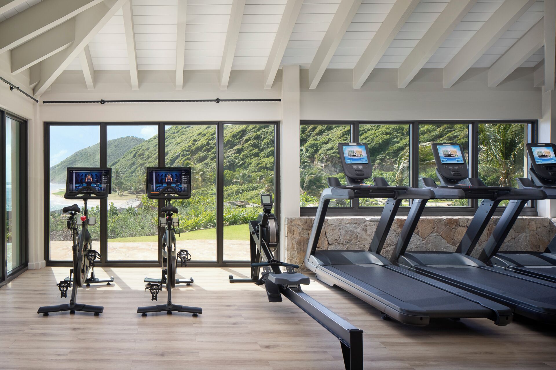A gym with exercise equipment, large windows, and a view of greenery.