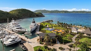 A marina with multiple yachts docked, a basketball court, and a pool area surrounded by greenery and palm trees. - Peter Island Resort (Sprat Bay)