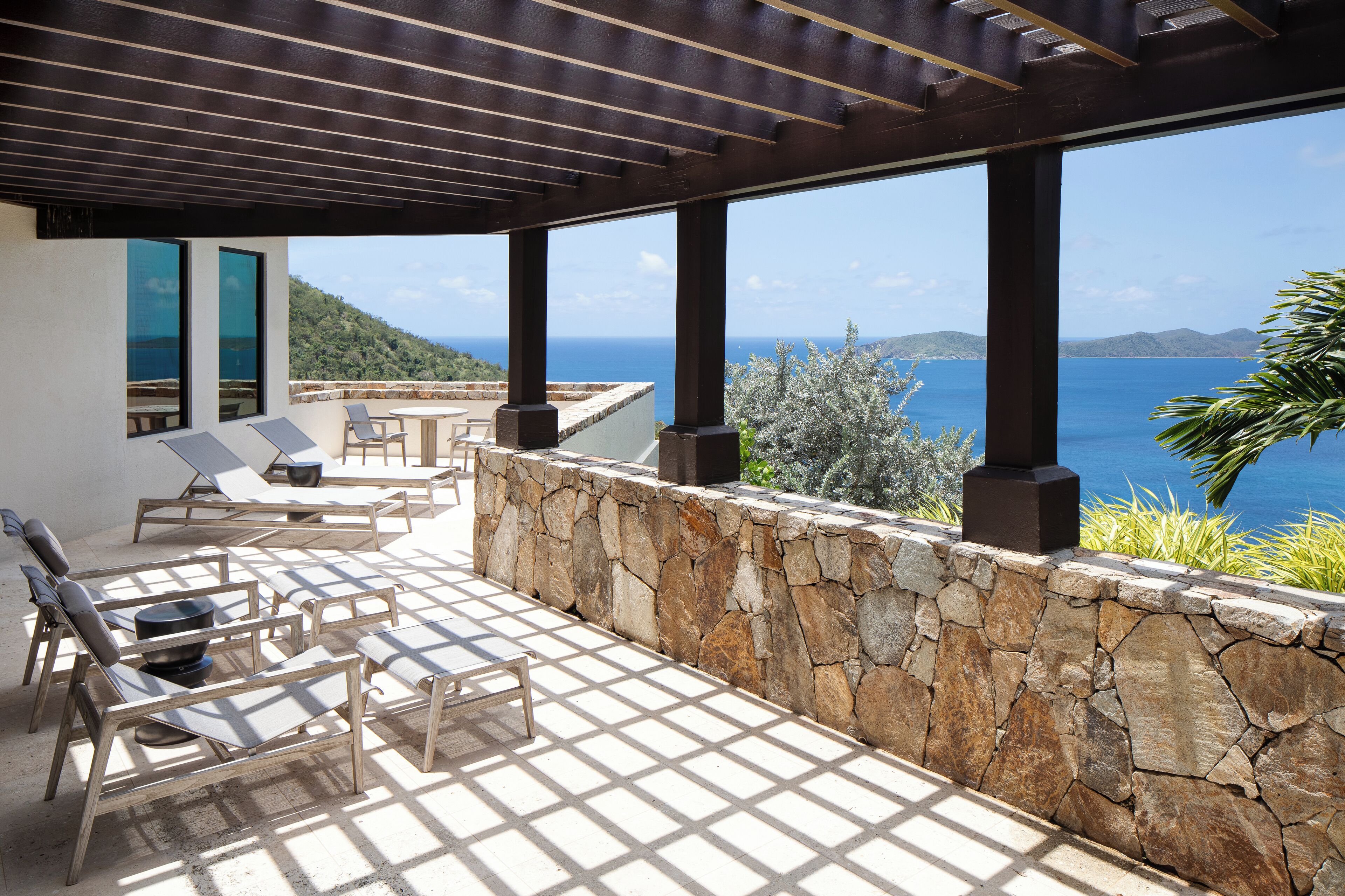 A covered outdoor seating area with stone walls and a view of the sea.
