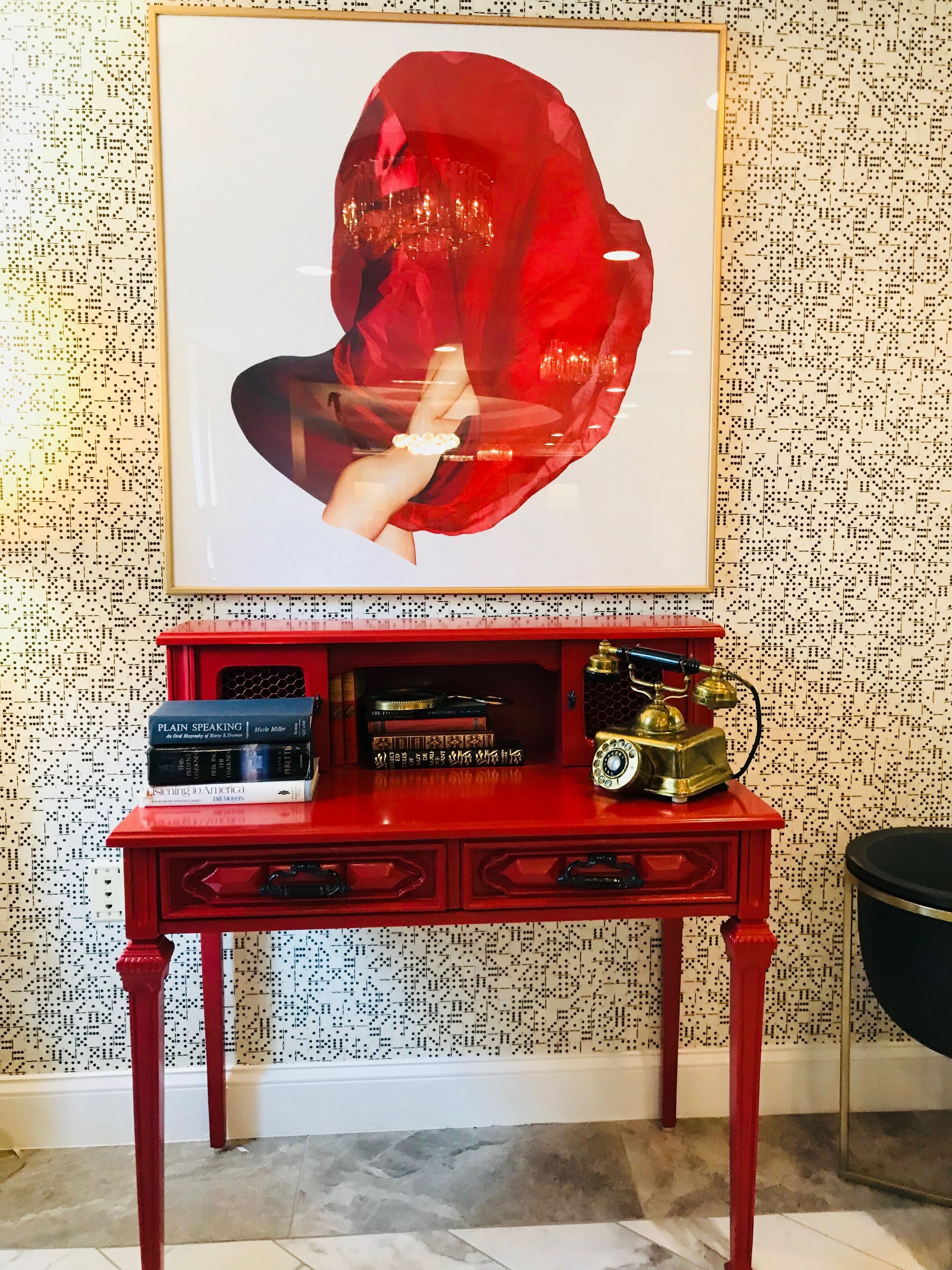Ein roter Holzbüro mit einem Bilderrahmen, der ein abstraktes Gemälde zeigt, einer Stapel Bücher und einem Vintage-Telefon.