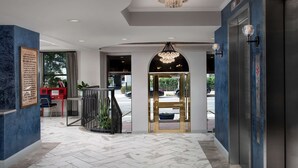A hotel lobby with a marble floor, a reception desk, a chandelier, and an elevator.