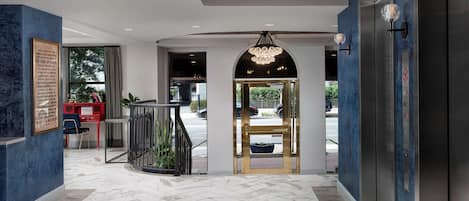 A hotel lobby with a marble floor, a reception desk, a chandelier, and an elevator.