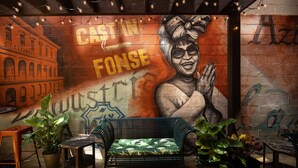 A mural with a woman and text, a green bench, and potted plants in a room with brick walls.