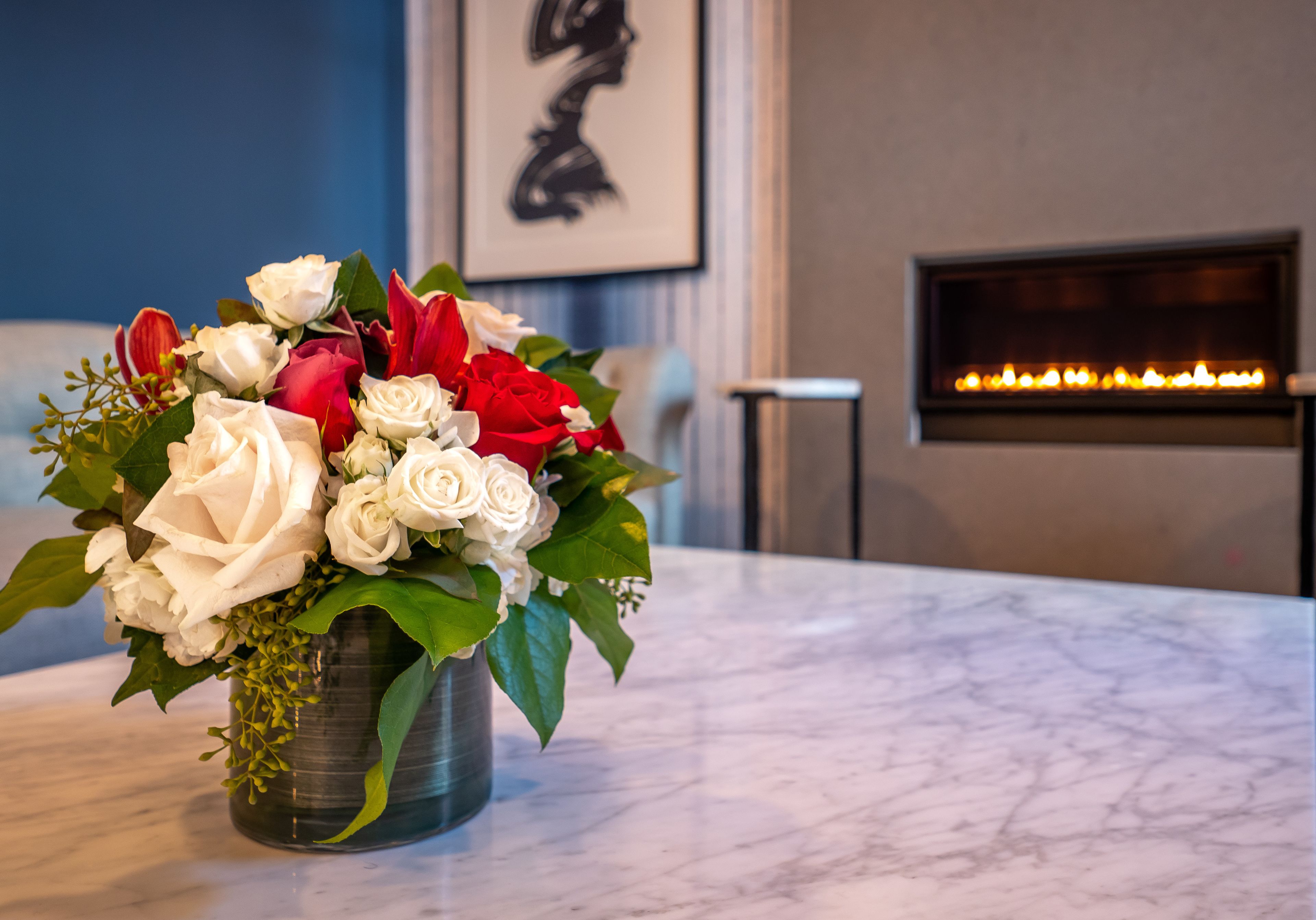 A marble table with a floral arrangement of white and red roses in a metal vase.