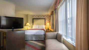 Habitación de hotel con cama, televisión, sofá y ventana con cortinas.