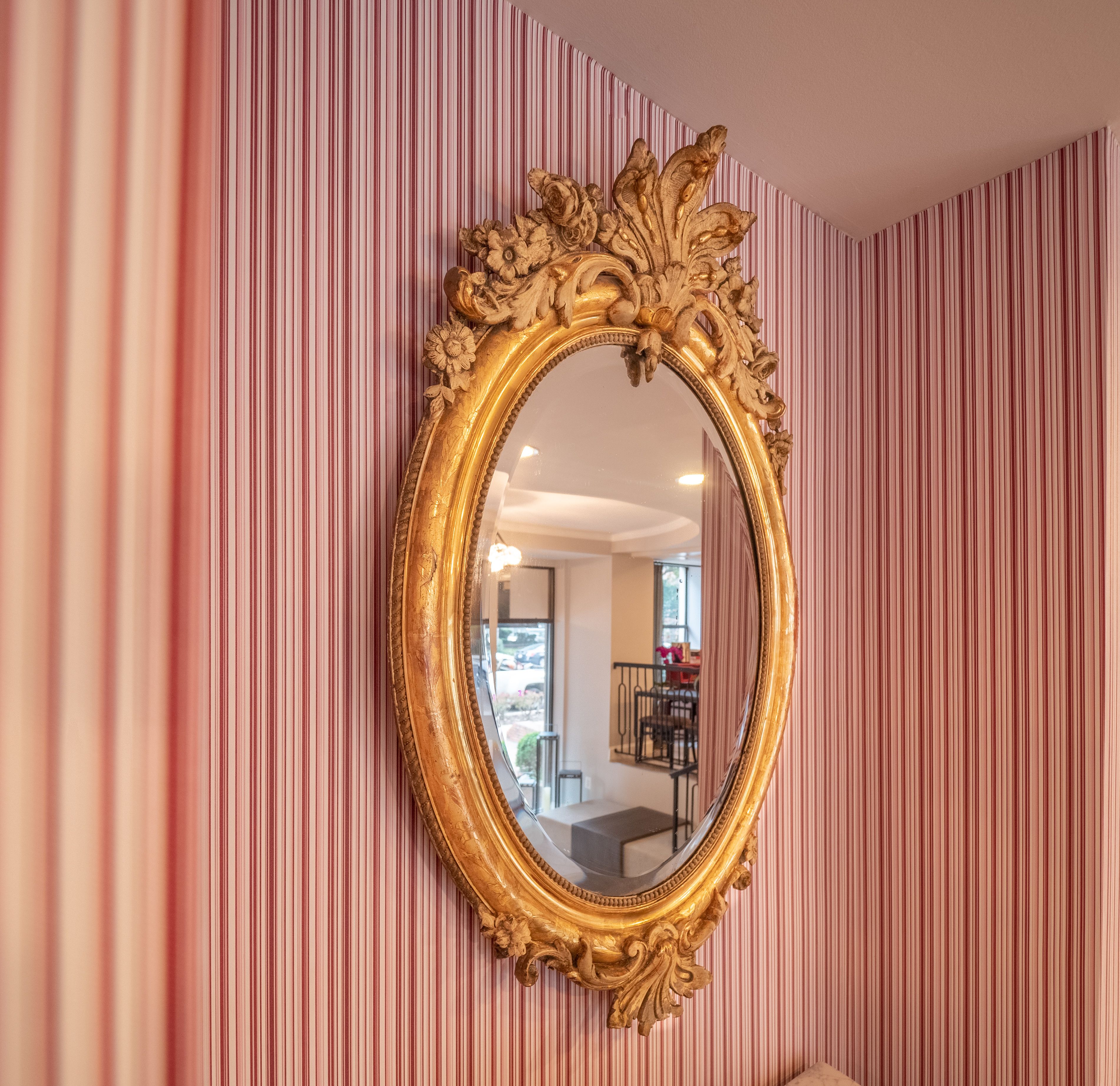 A room with a large ornate gold-framed mirror on a striped wall.