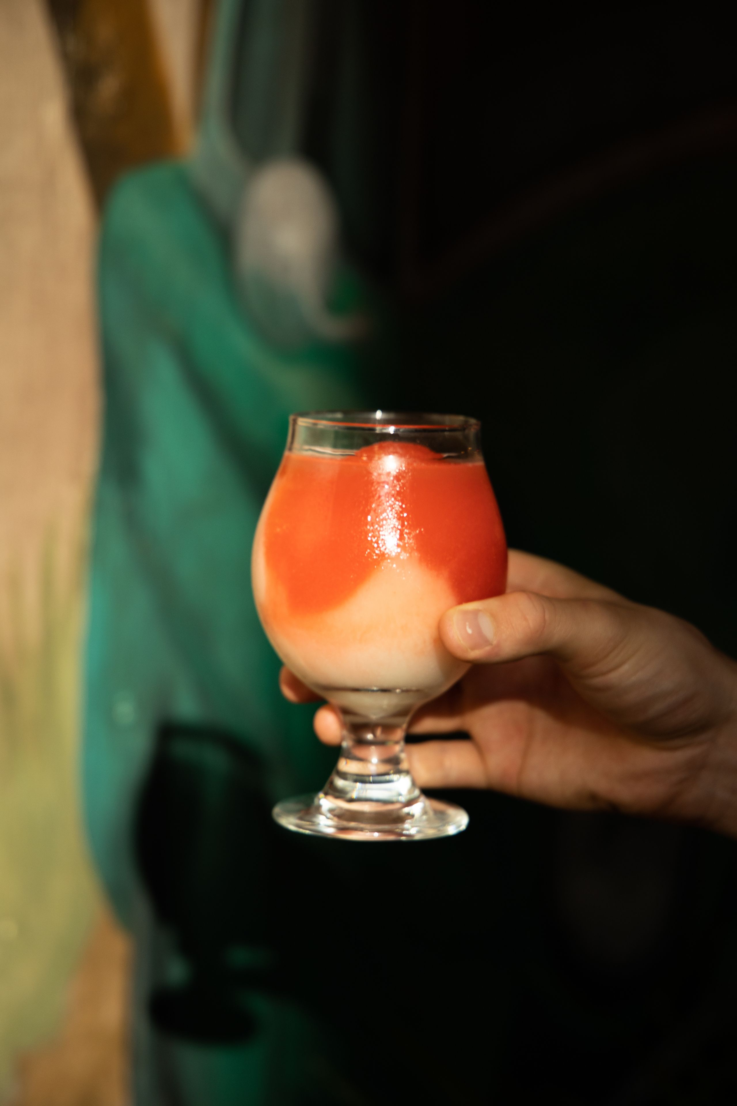 Een hand die een glas met een gelaagde drank vasthoudt.