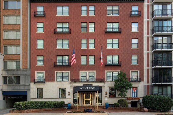 A multi-story hotel with a red brick facade, multiple balconies, and flags. - West End Washington DC, Tapestry Collection by Hilton (Washington)