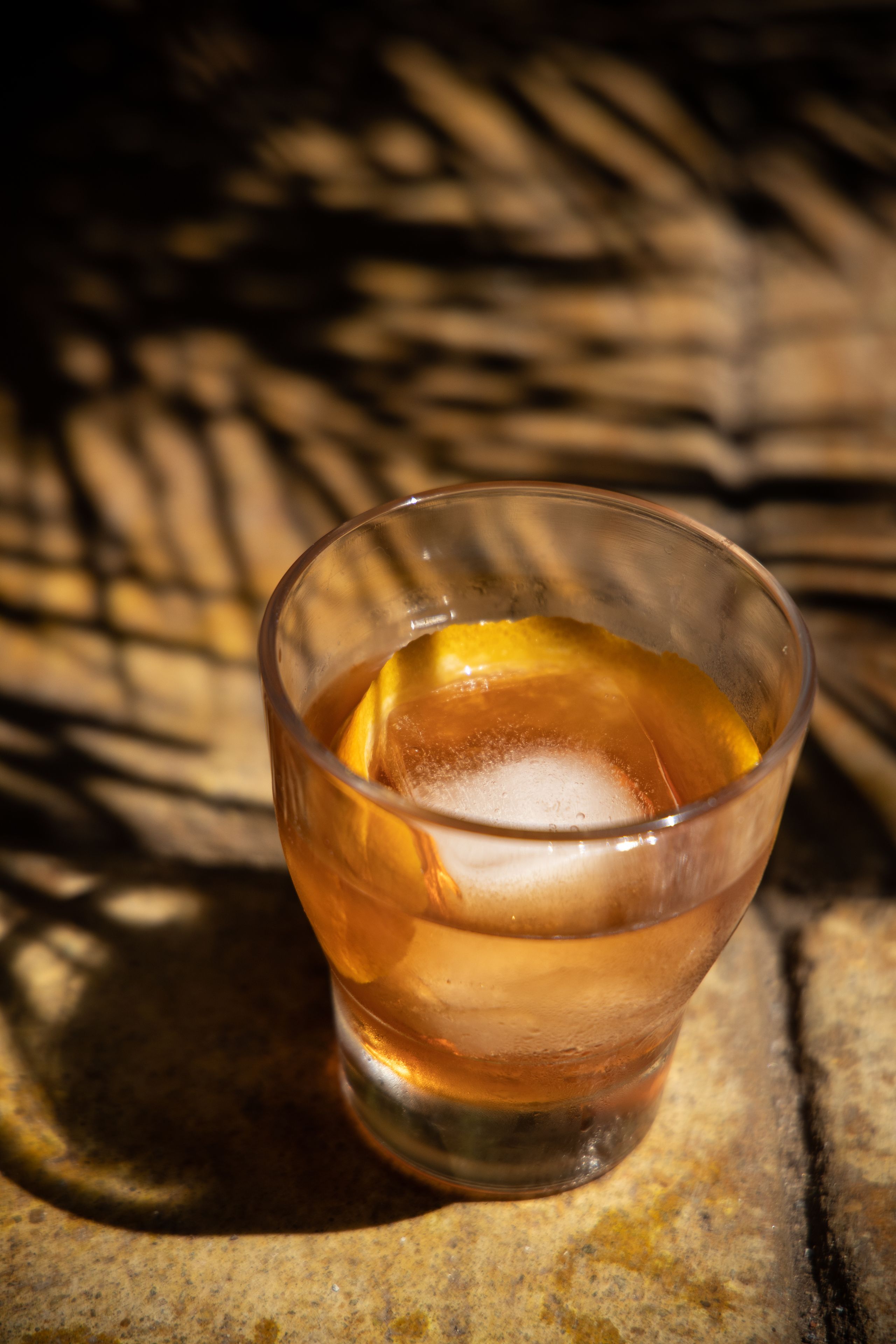 A glass with a beverage and ice on a textured surface.