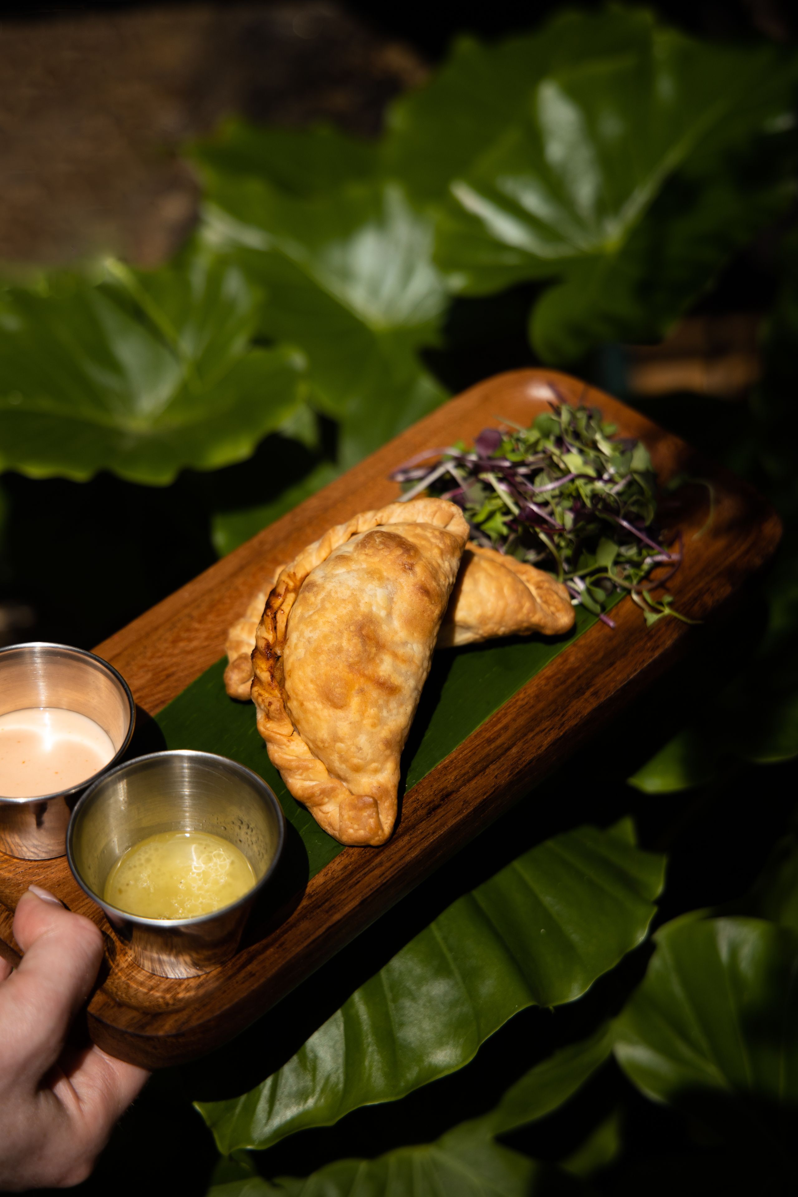 A wooden serving tray with two pastries and a small bowl of sauce.