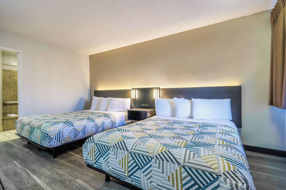 Une chambre d’hôtel avec deux lits, une table de chevet et un luminaire fixé au mur.