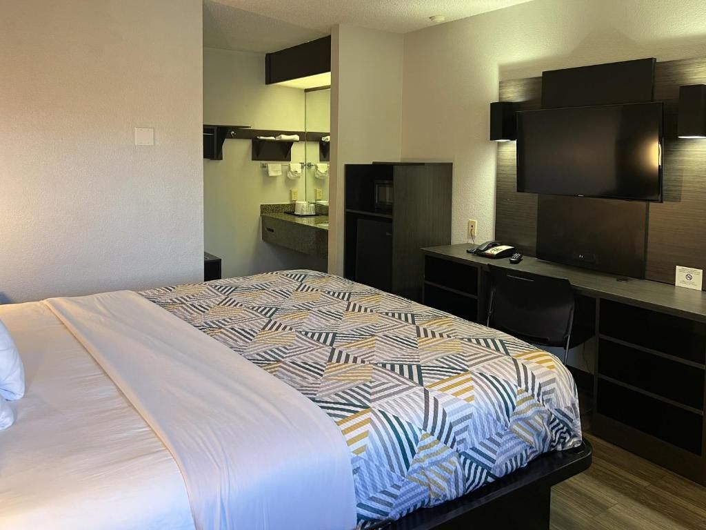 A hotel room with a bed, a desk, a flat-screen TV, and a mirror.